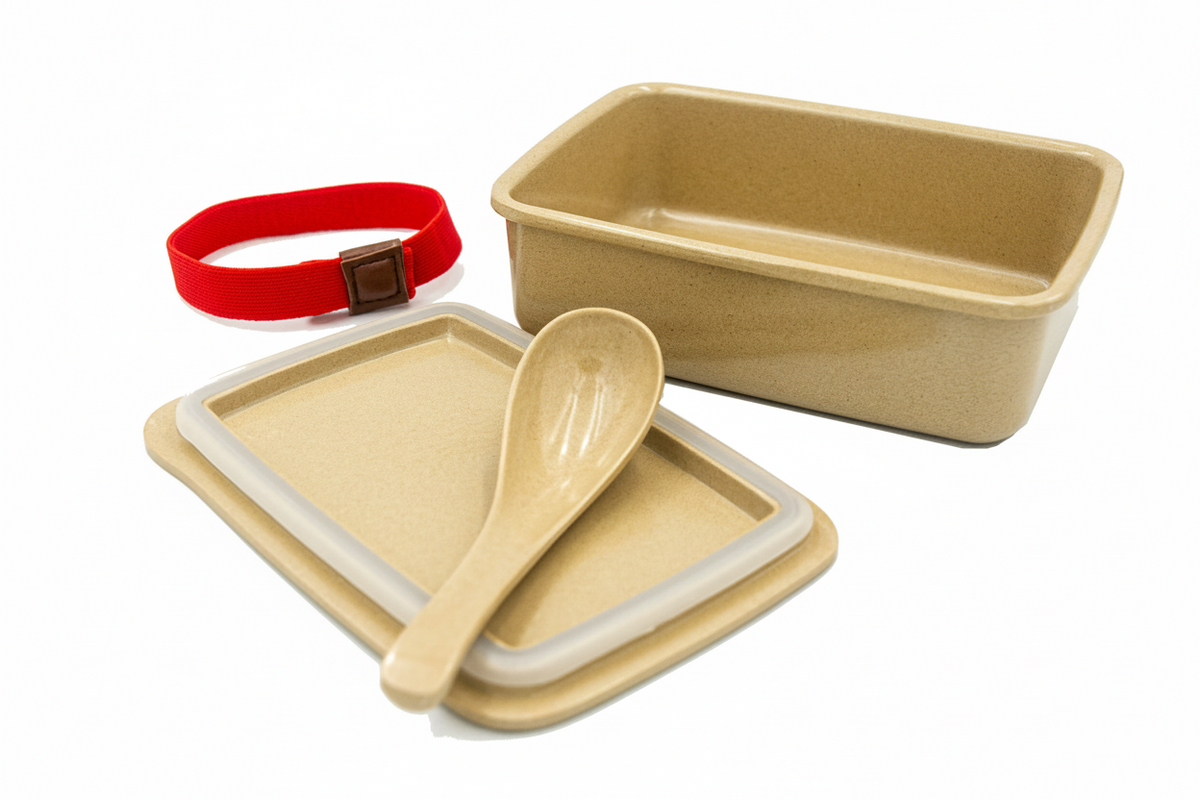 A set of beige bamboo-style lunch containers and utensils on a white background, including a rectangular container, a square lid with a beige rim, a small spoon, and a red wrist strap.