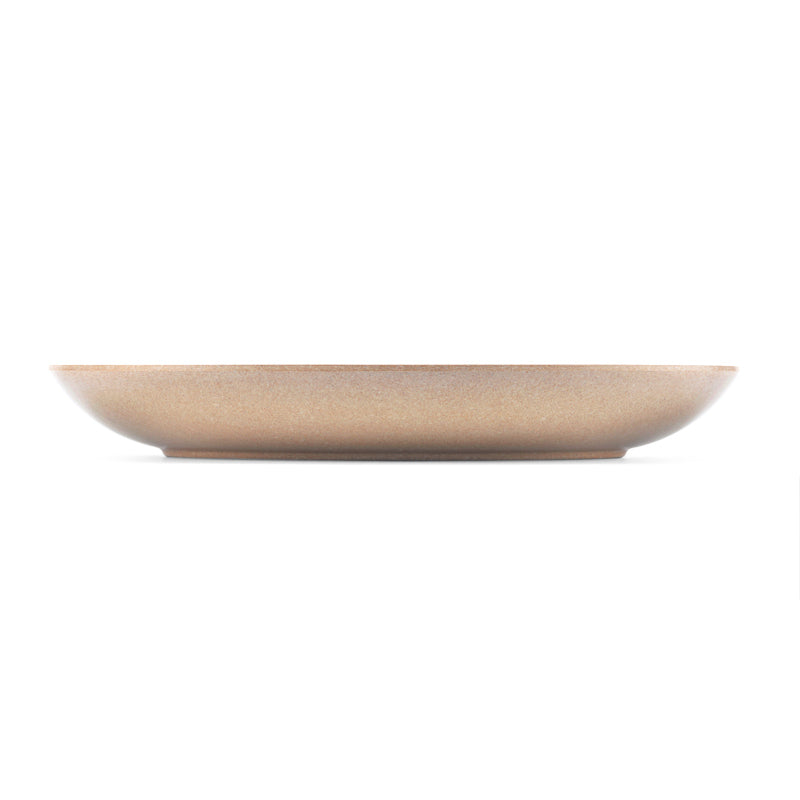 A shallow, wide ceramic plate with a speckled beige finish, shown from a direct side profile against a solid white background.
