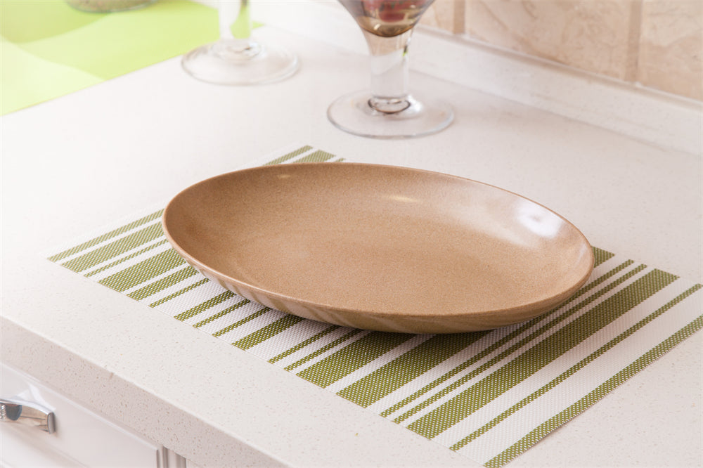 A shallow oval ceramic plate in a warm beige color, resting on a green and white striped placemat on a white countertop.