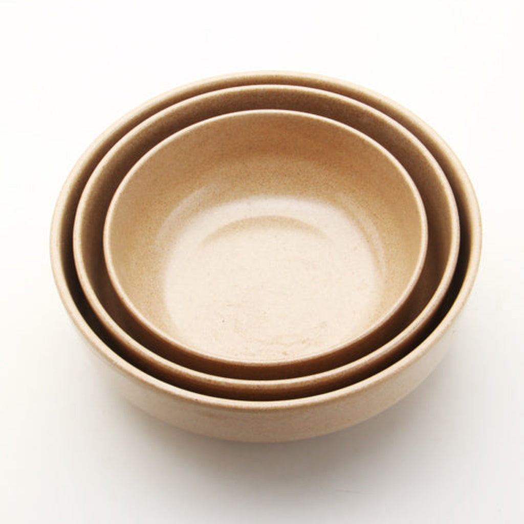 Three nested ceramic bowls in a warm sandy beige color, photographed from a top-down angle on a clean white background.