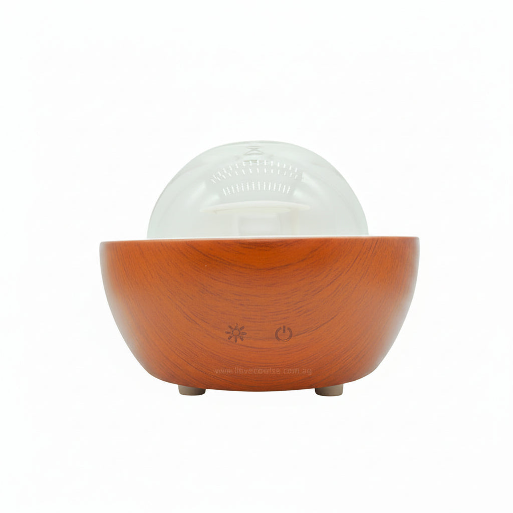 A modern tabletop diffuser with a warm brown wood-grain bowl base, a clear glass dome, and small gray feet, shown on a plain white background.