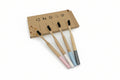Four bamboo toothbrushes with colorful handles in pink, white, light blue, and dark gray, arranged in front of a brown cardboard box on a white background.
