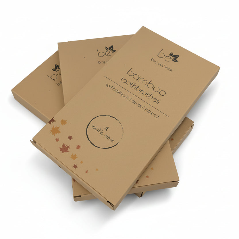 Four kraft paper boxes of bamboo toothbrushes stacked on a light gray background. The boxes feature a minimalist black logo and text, with one box decorated with small orange and yellow leaf illustrations.
