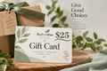 A BuyEcoWise $25 gift card displayed on a wooden surface in front of a kraft gift box tied with a green ribbon. The card has a white and light green design with leaf illustrations and the text 'Give Good Choices' printed on the scene.