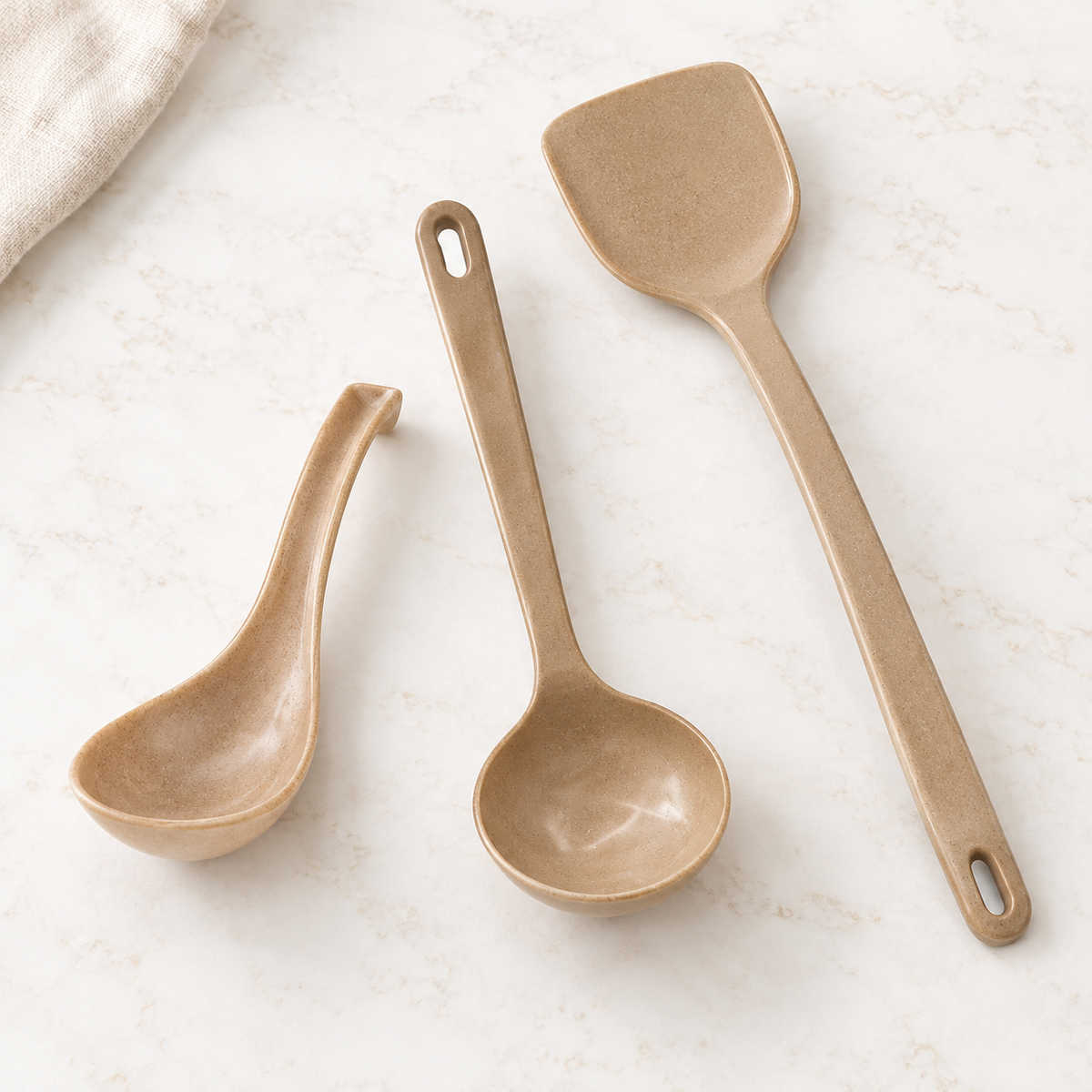 HUSKSWARE rice-husk serving spoon, ladle and spatula arranged on a pale stone surface in soft daylight.